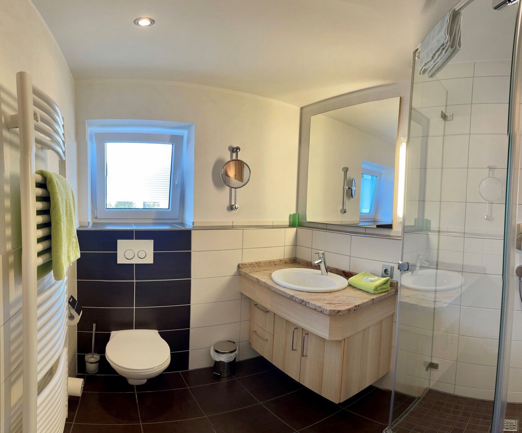 A modern bathroom with a toilet, two sinks, a shower, and a window.