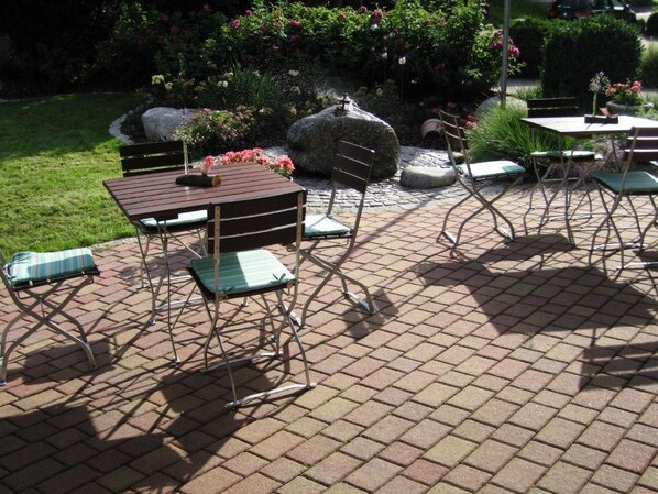 Un área de patio al aire libre con piso de ladrillo, sillas de metal y una mesa de madera.