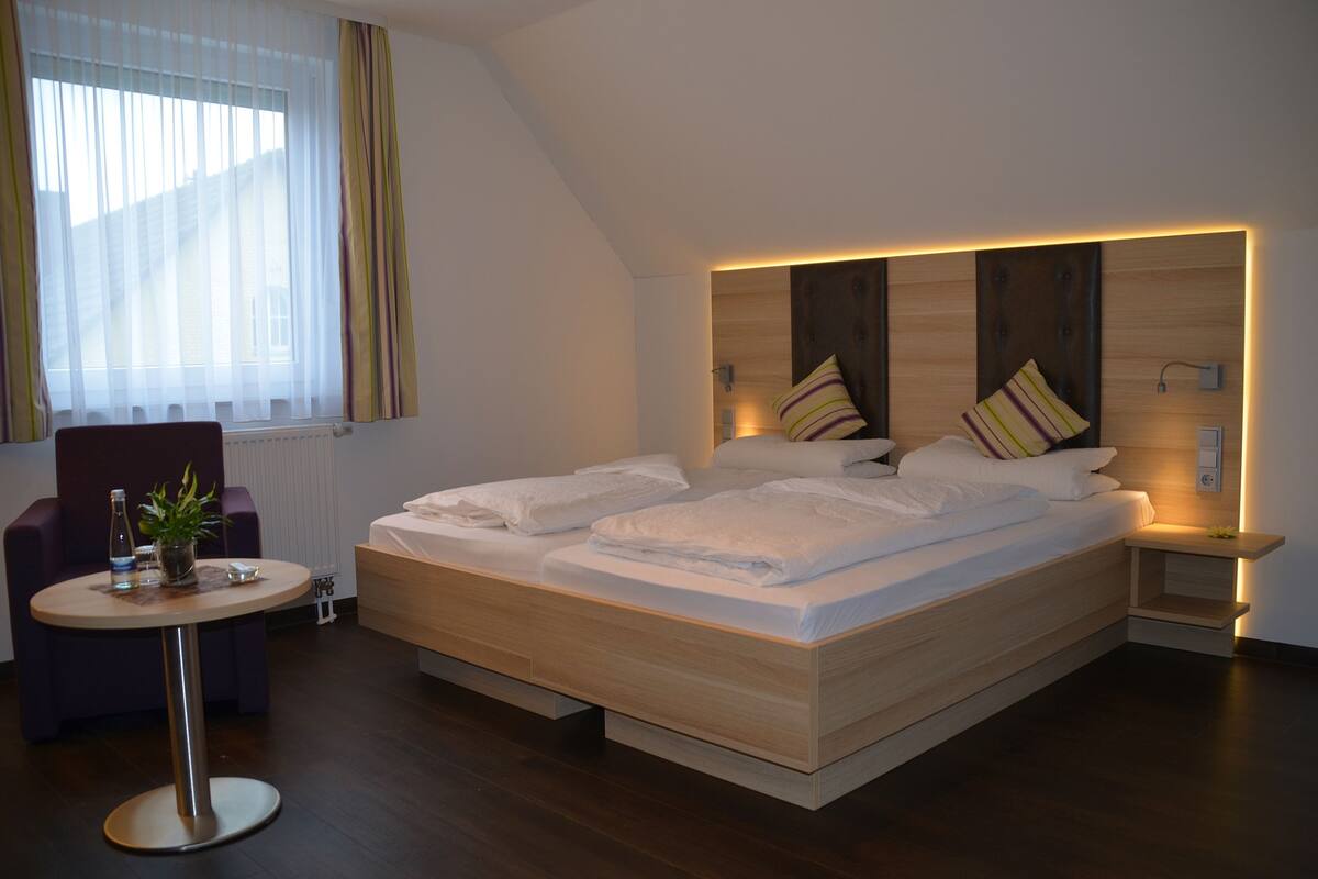 A modern hotel room with a large bed, a small round table with a plant, and a chair.