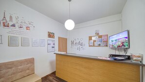 A reception area with a wooden counter, a bench, and various wall decorations including travel-themed artwork and framed certificates. - Hostel Orange (Prague)