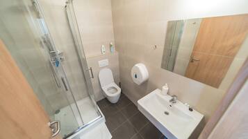 Un baño moderno con ducha de vidrio, inodoro y lavamanos con espejo.
