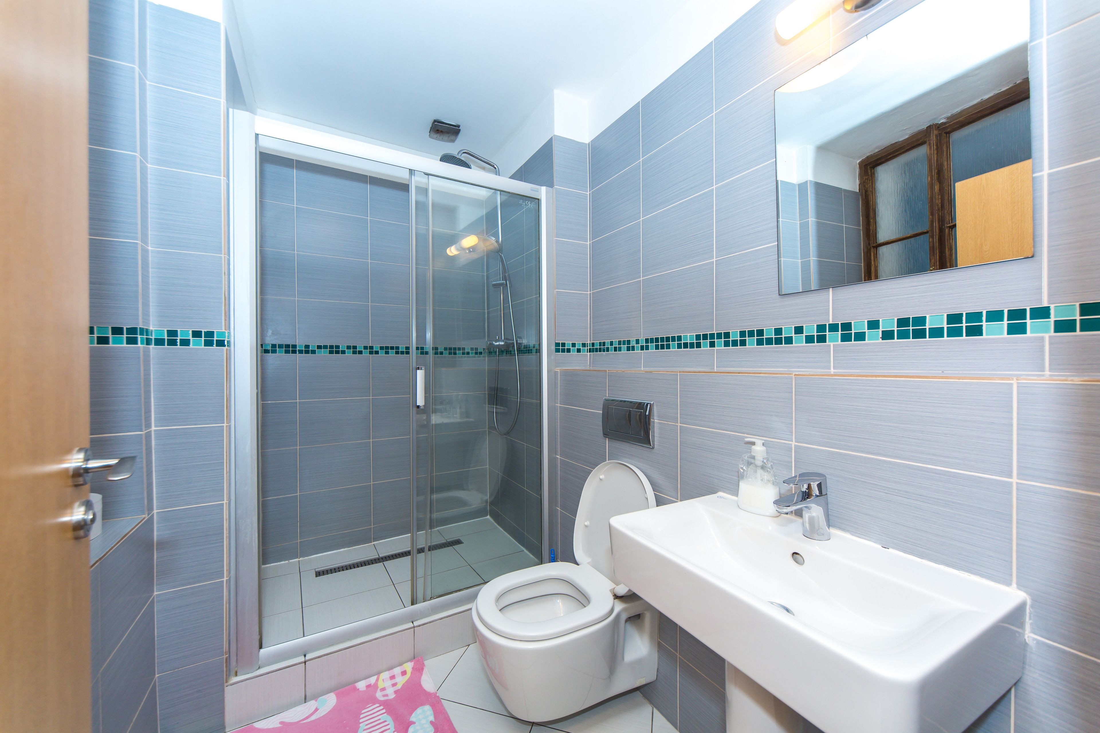 A bathroom with a glass shower enclosure, a toilet, and a sink with a mirror above it.