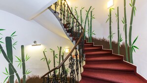 A staircase with red carpet and decorative metal railings, surrounded by wall art depicting bamboo. - Hostel Orange (Prague)