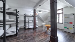 A dormitory room with bunk beds, a wooden table, white chairs, and a window with lockers. - Hostel Orange (Prague)