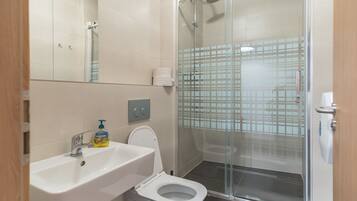 Un baño moderno con cabina de ducha de vidrio, un lavabo blanco y un inodoro.