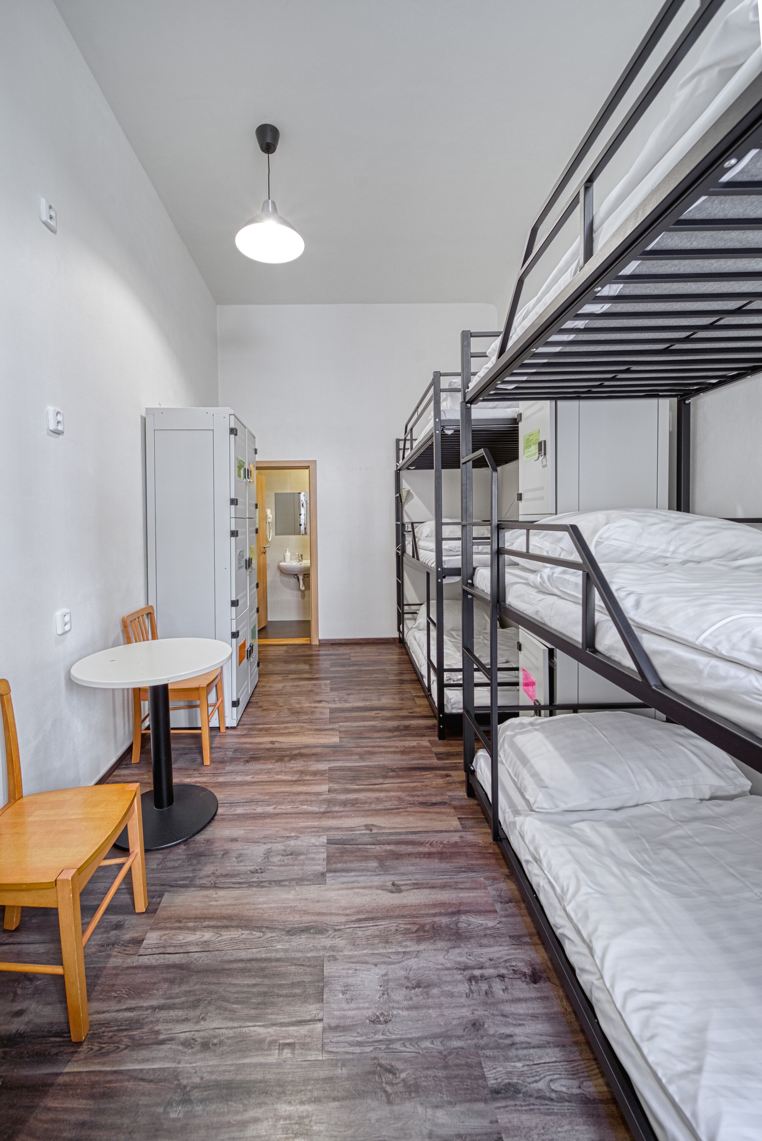 A dormitory room with bunk beds, a wooden table, and a chair.