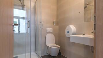 Un baño moderno con cabina de ducha de vidrio, inodoro, lavabo y espejo.
