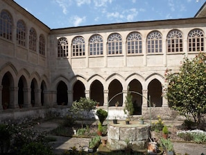 Ein Innenhof mit einem Brunnen, umgeben von Steingewölben und Topfpflanzen.