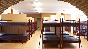 Een slaapzaal met opstelling van stapelbedden in rijen, houten vloer en een stenen boog.