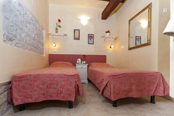 A room with two beds, a nightstand, a mirror, and wall-mounted shelves with decorative items.