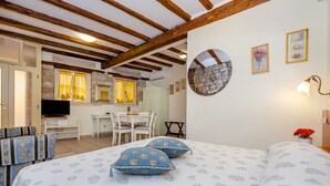 Een slaapkamer met een bed, kussens, een televisie, een bureau en een stoel.