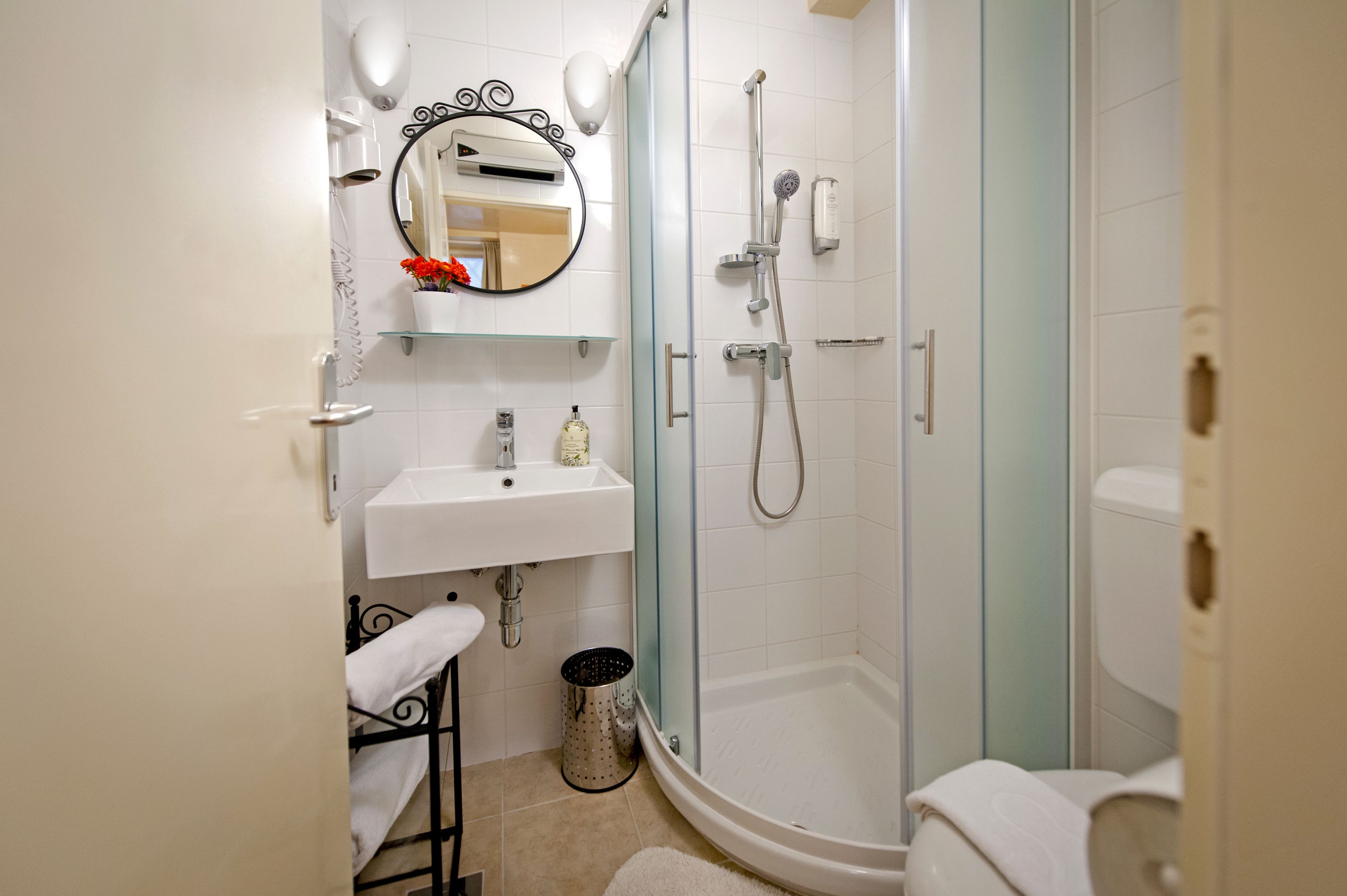 Un baño con ducha envuelta en vidrio, un lavamanos blanco, un espejo con marco decorativo y un pequeño cubo de basura.