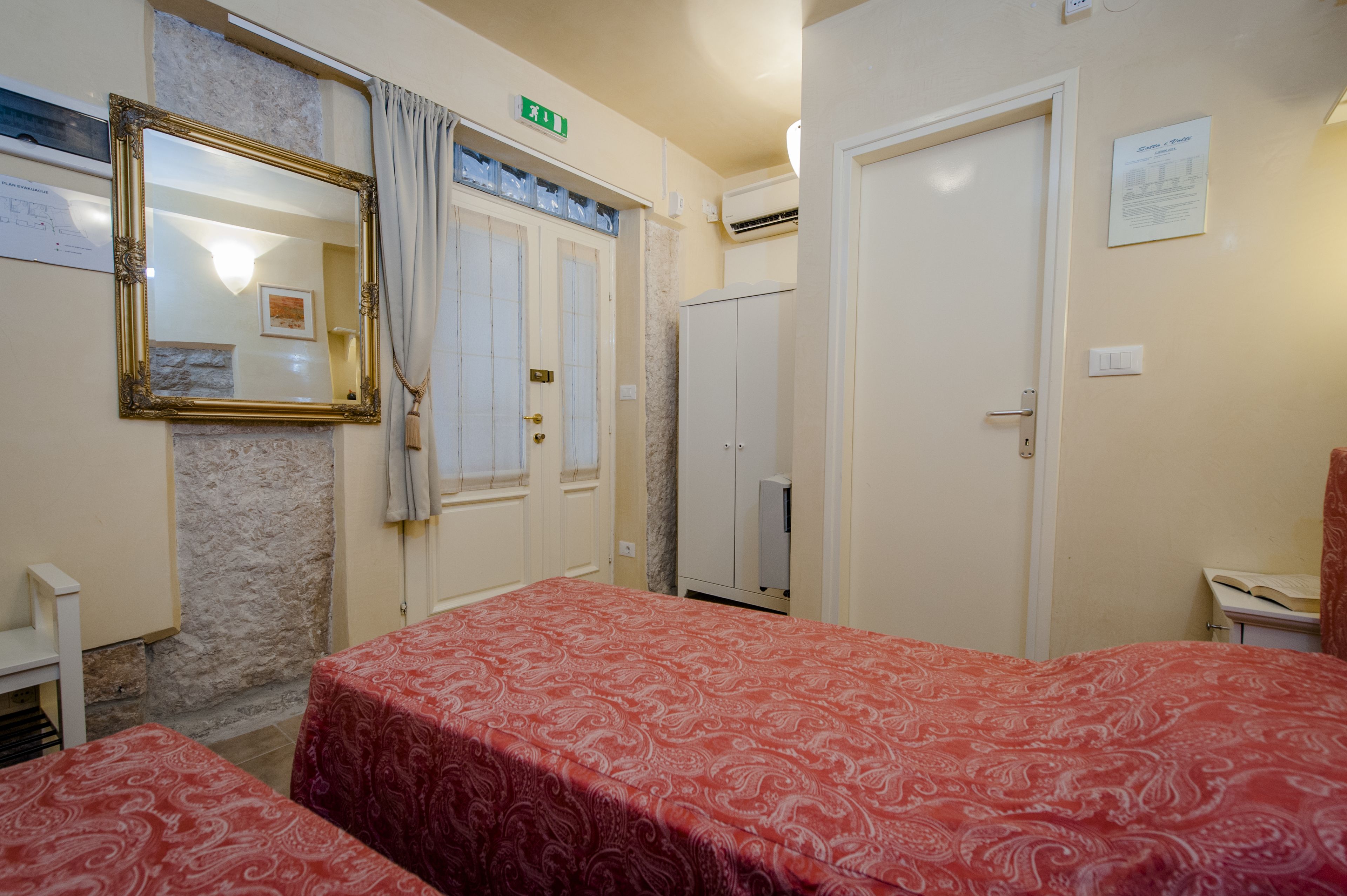 A hotel room with two beds, a large mirror, a wardrobe, and an exit sign.