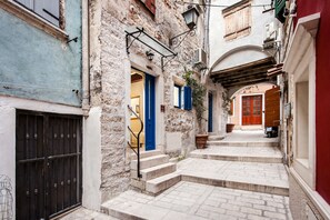 A narrow street with stone buildings, a wooden door, and a metal gate.