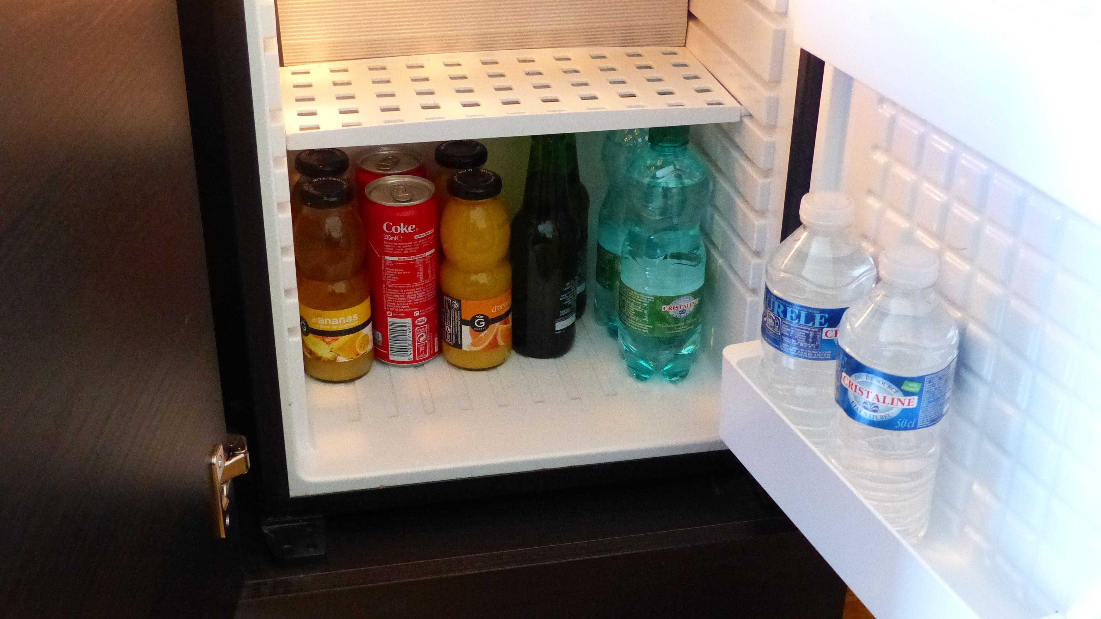 A refrigerator with various beverages including soda cans, bottles of water, and a bottle of juice.
