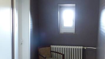 Ein Zimmer mit Heizkörper, Fenster, Stuhl und fußbodenmuster.