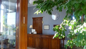 A reception desk with a clock, framed menu, and a plant. - Hôtel de l'Europe (Toul)