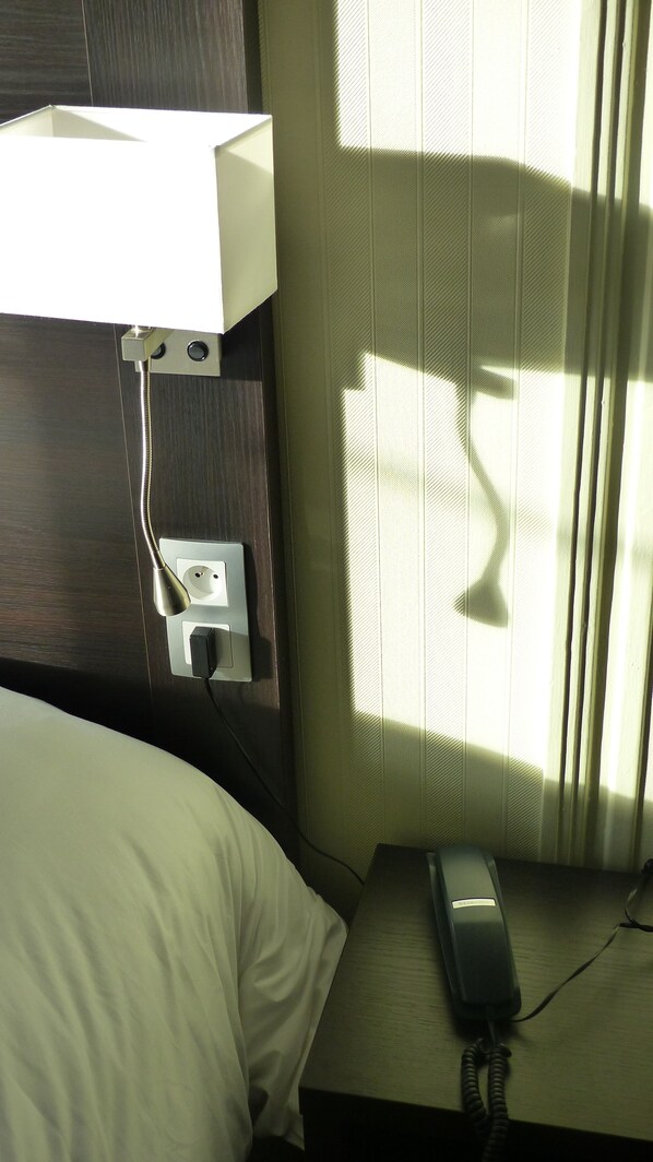 Una habitación de hotel con cama, mesita de noche y toma de corriente.
