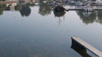 A calm water body with boats docked, a wooden dock, and buildings in the background.