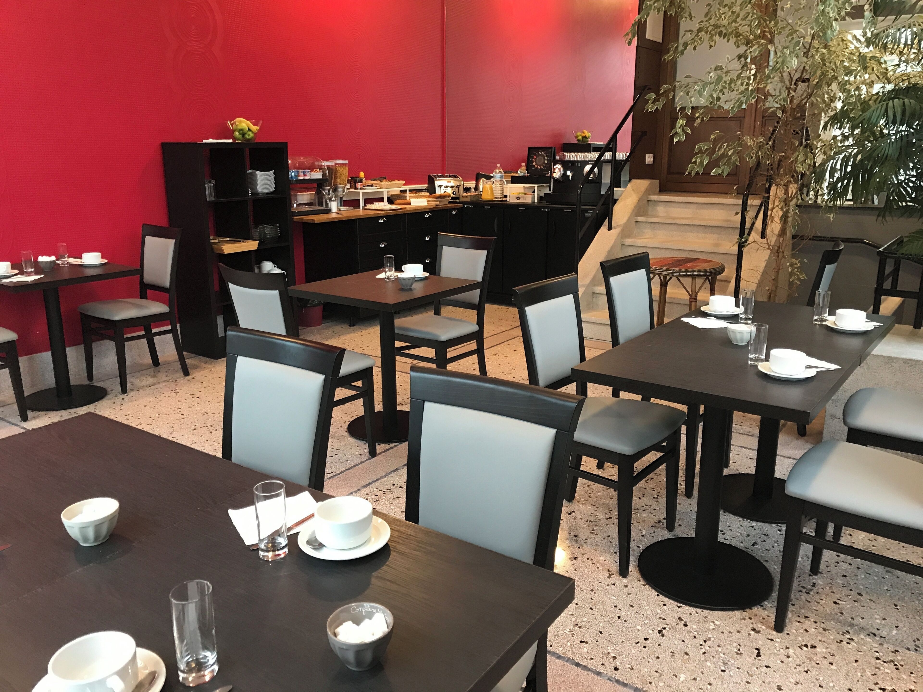 A restaurant with multiple tables and chairs, a red wall, and a staircase leading to an upper level.