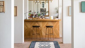 Un intérieur comprenant un espace bar, des tabourets de bar en bois, un tapis à motifs et des lampes suspendues.