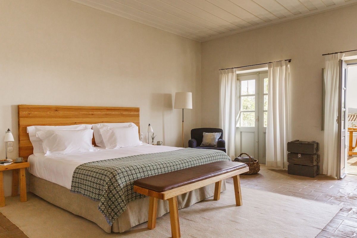 Ein Schlafzimmer mit einem hölzernen Bett, einer Bank, einem Sessel und einem kleinen Tisch mit Lampe.