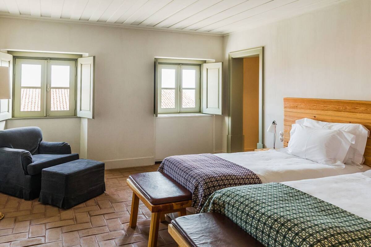 Ein Zimmer mit zwei Betten, einem Schlafsofa, einer Sitzbank und zwei Fenstern.