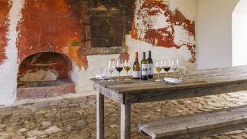 A rustic interior with a wooden table displaying wine bottles and glasses, a stone floor, and a weathered wall with peeling paint.