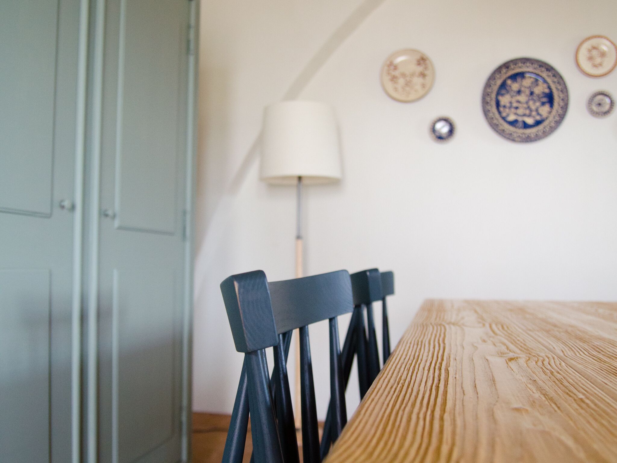 Un coin repas avec une table et des chaises en bois, une lampe et des assiettes décoratives accrochées au mur.