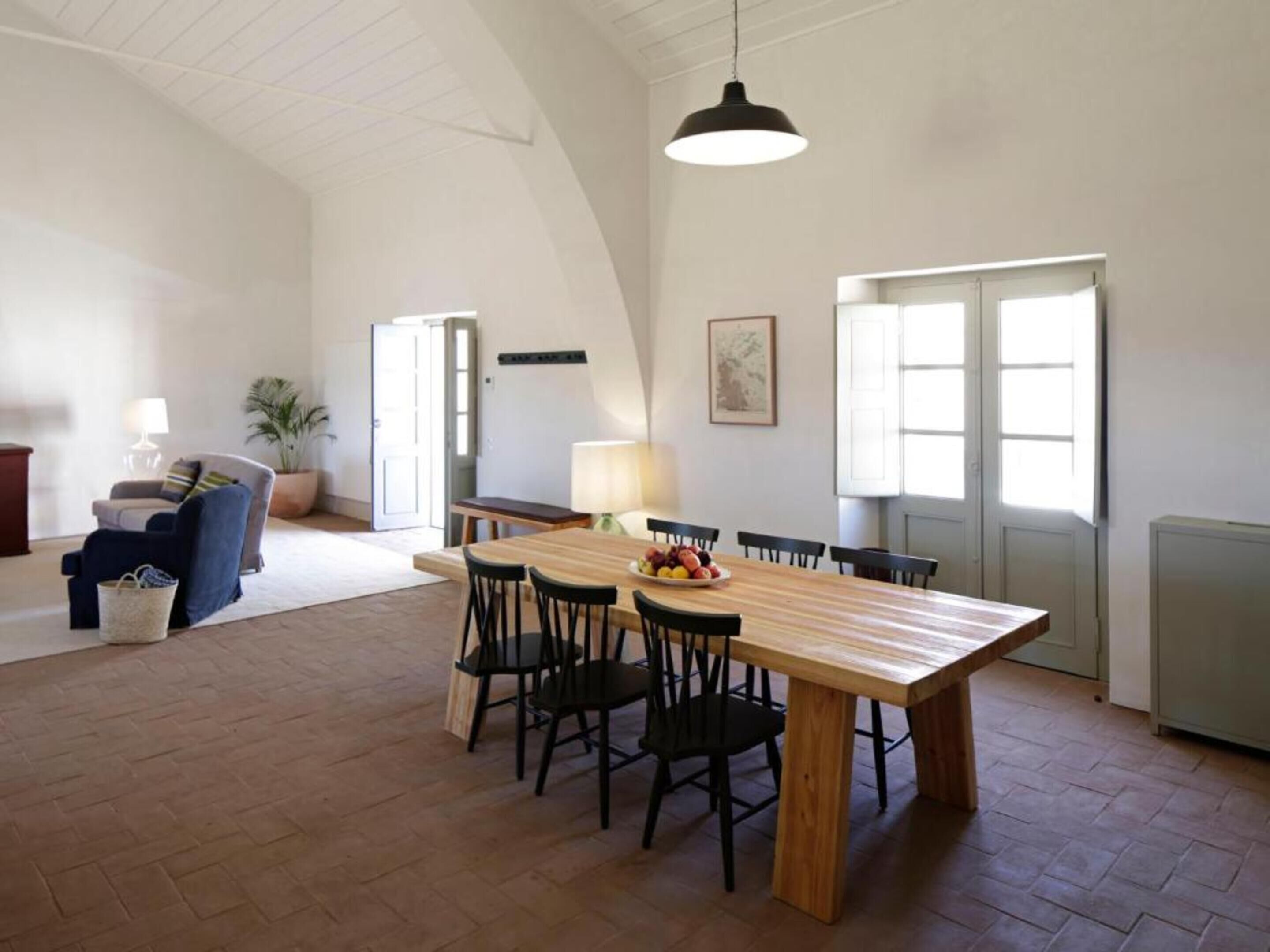 Un comedor amplio con una mesa y sillas de madera, una lámpara colgante y vistas al exterior a través de grandes ventanales.