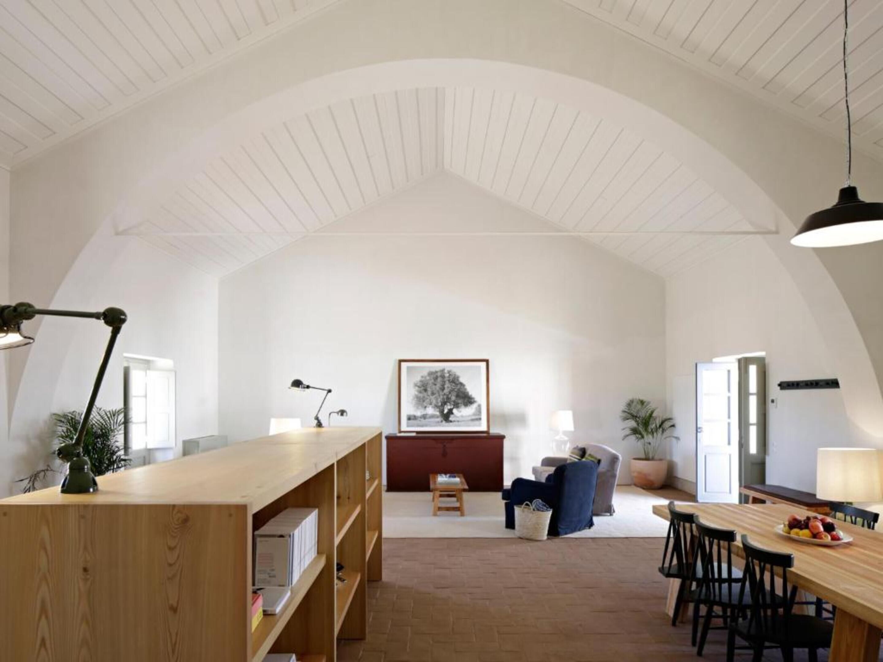 Una habitación amplia con un alto techo abovedado, muebles de madera y un comedor con sillas y una mesa.