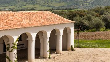 A building with a tiled roof and arches, set against a hilly landscape with a castle in the background.