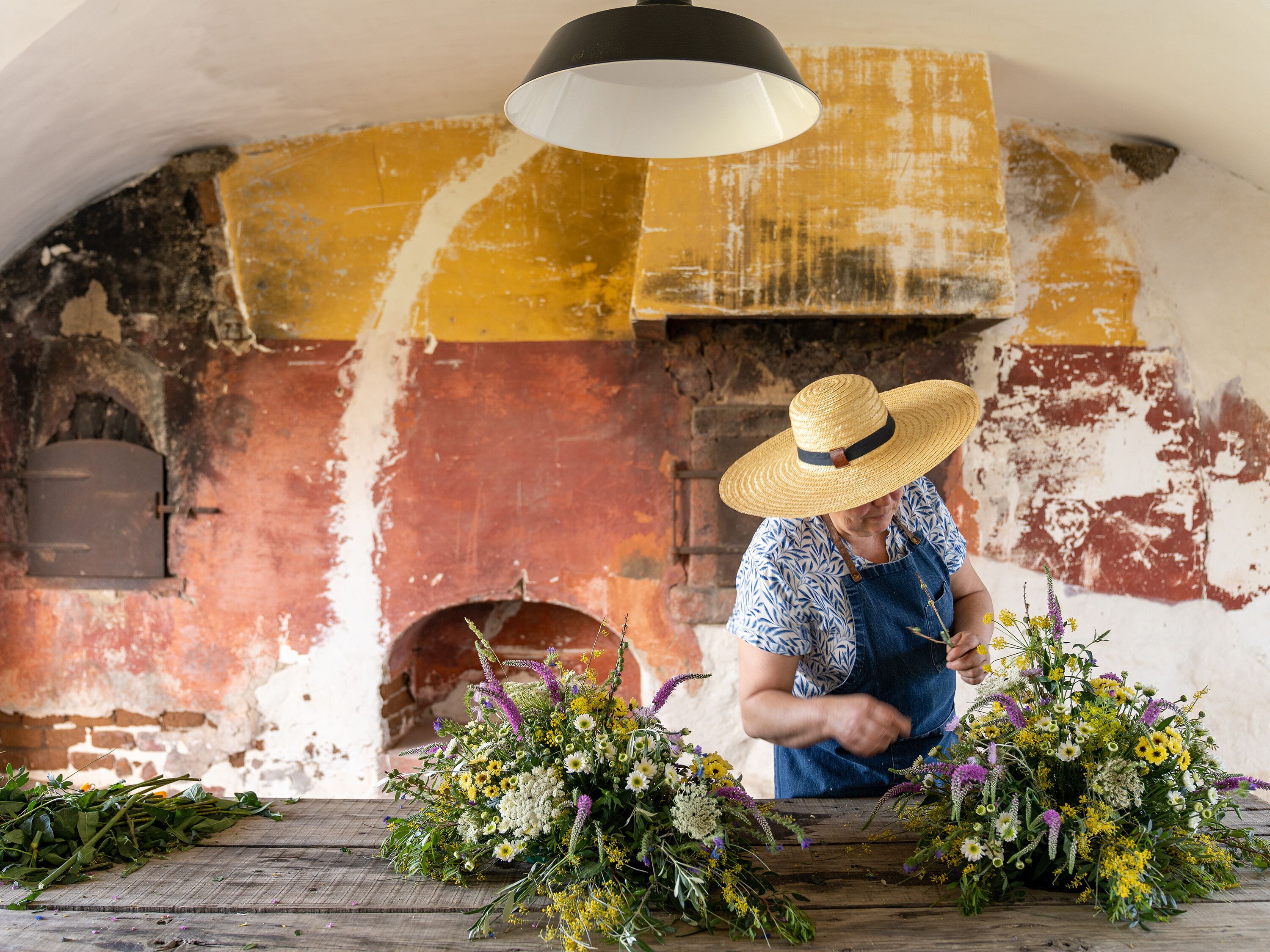 A person arranging flowers in a rustic setting with a brick wall and a wooden table.