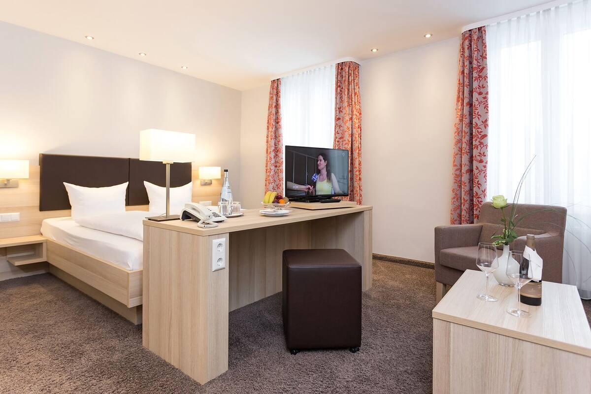 A hotel room with a bed, desk, TV, and seating area.