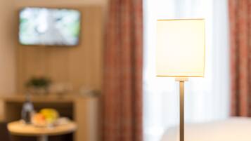 A room with a television on the wall, a table with items on it, and a lamp with a blank screen.