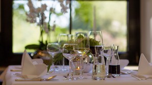 Une table dressée pour le dîner, avec de beaux verres et une bougie, placée près d’une fenêtre donnant sur un paysage verdoyant.