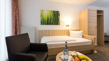 Habitación de hotel con cama, una silla, mesita de noche con botella de agua y fruta, y lámpara de pared.