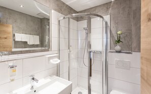 Une salle de bain moderne avec une douche à parois de verre, un lavabo blanc et un miroir au-dessus du lavabo.