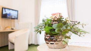 Une pièce avec une table ronde en bois, un pot de fleurs contenant différentes plantes et fleurs, un téléviseur accroché au mur et une chaise blanche.