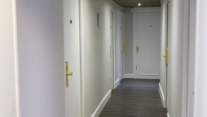 A long, narrow hallway with white walls and dark wooden flooring, leading to multiple doors with gold handles. - ABC Hôtel (Toul)