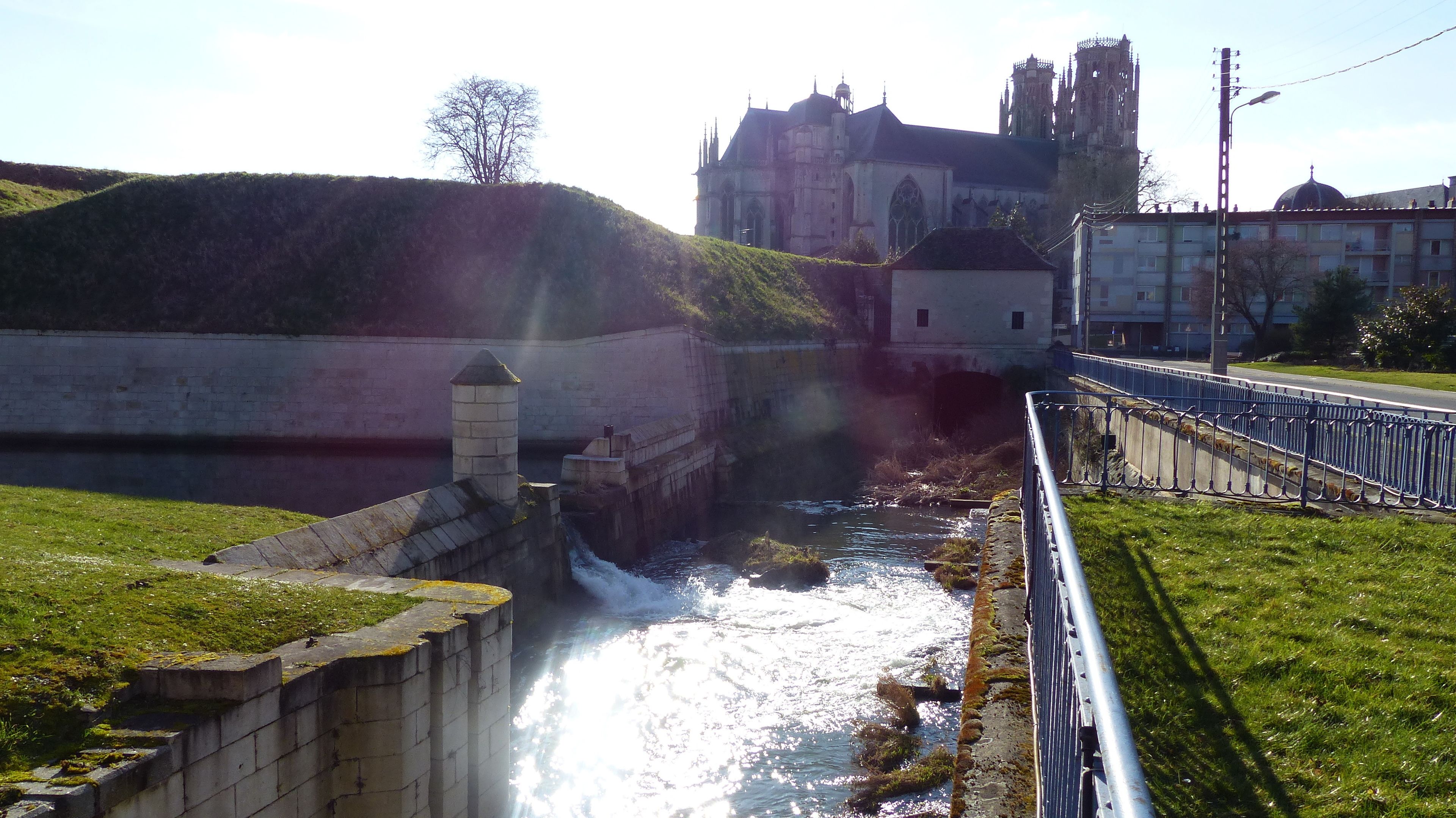 A river flowing through a stone bridge with a historic building in the background.