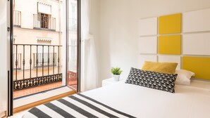 A bedroom with a bed, a view of a balcony, and a yellow accent wall. - Smartr Madrid Chueca  (Madrid)