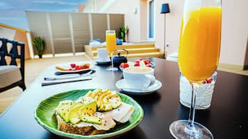 Desayuno con tostadas, fruta y un vaso de zumo de naranja sobre una mesa.