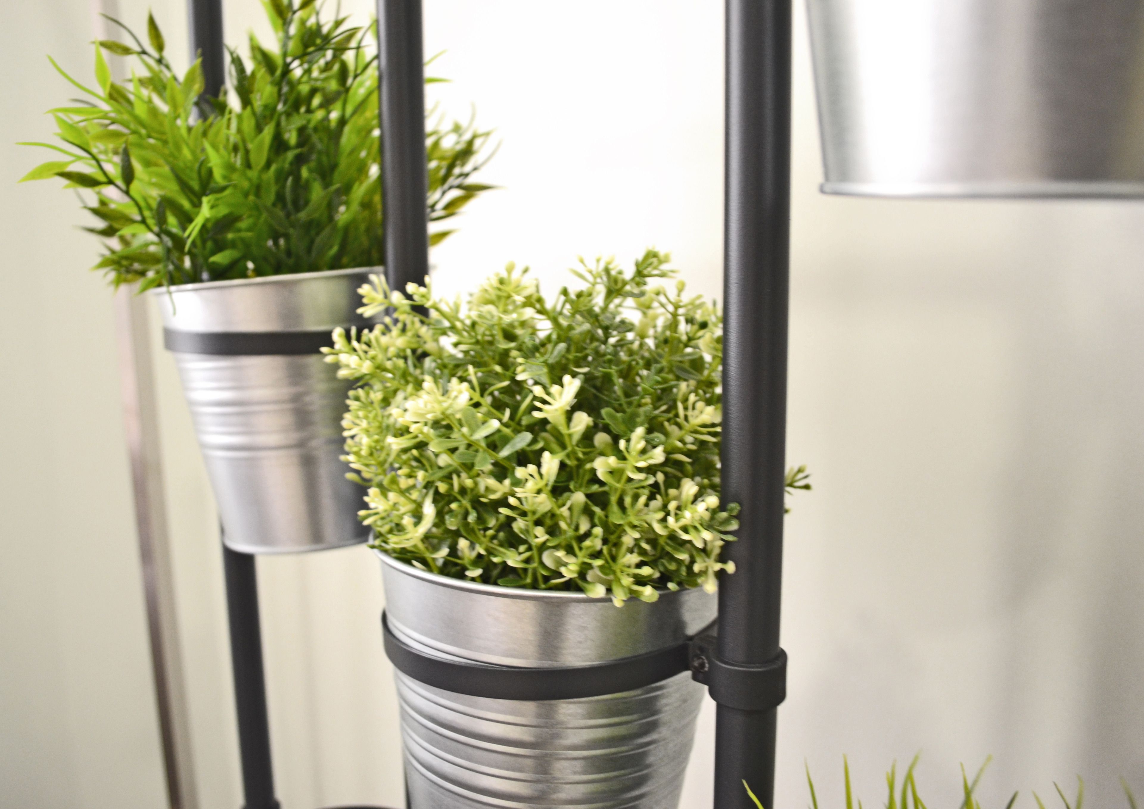 Two potted plants in metal containers mounted on a black metal stand.