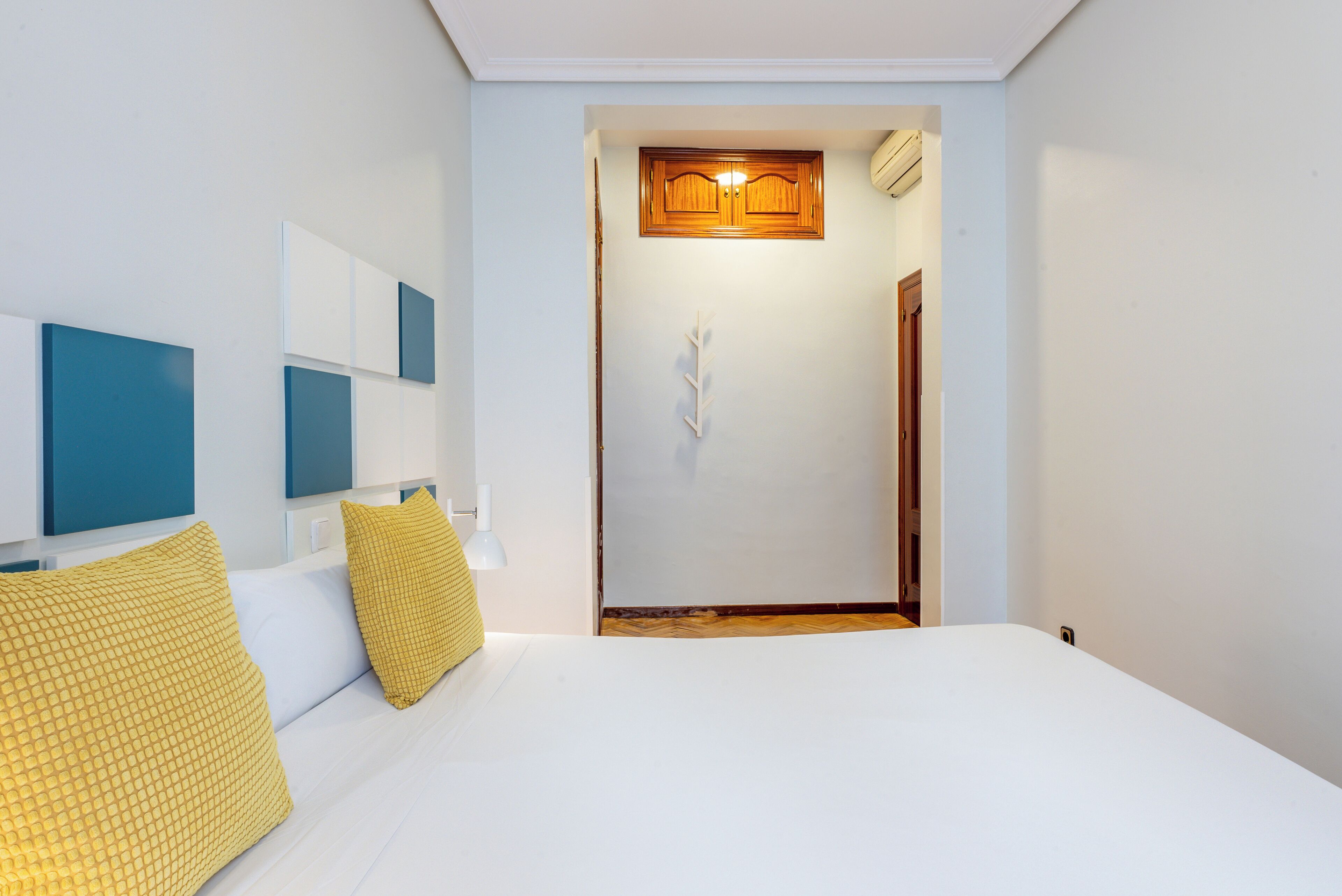 Ein Hotelzimmer mit einem Bett, einer Holztür und einer weißen Wand mit Lichtschalter.