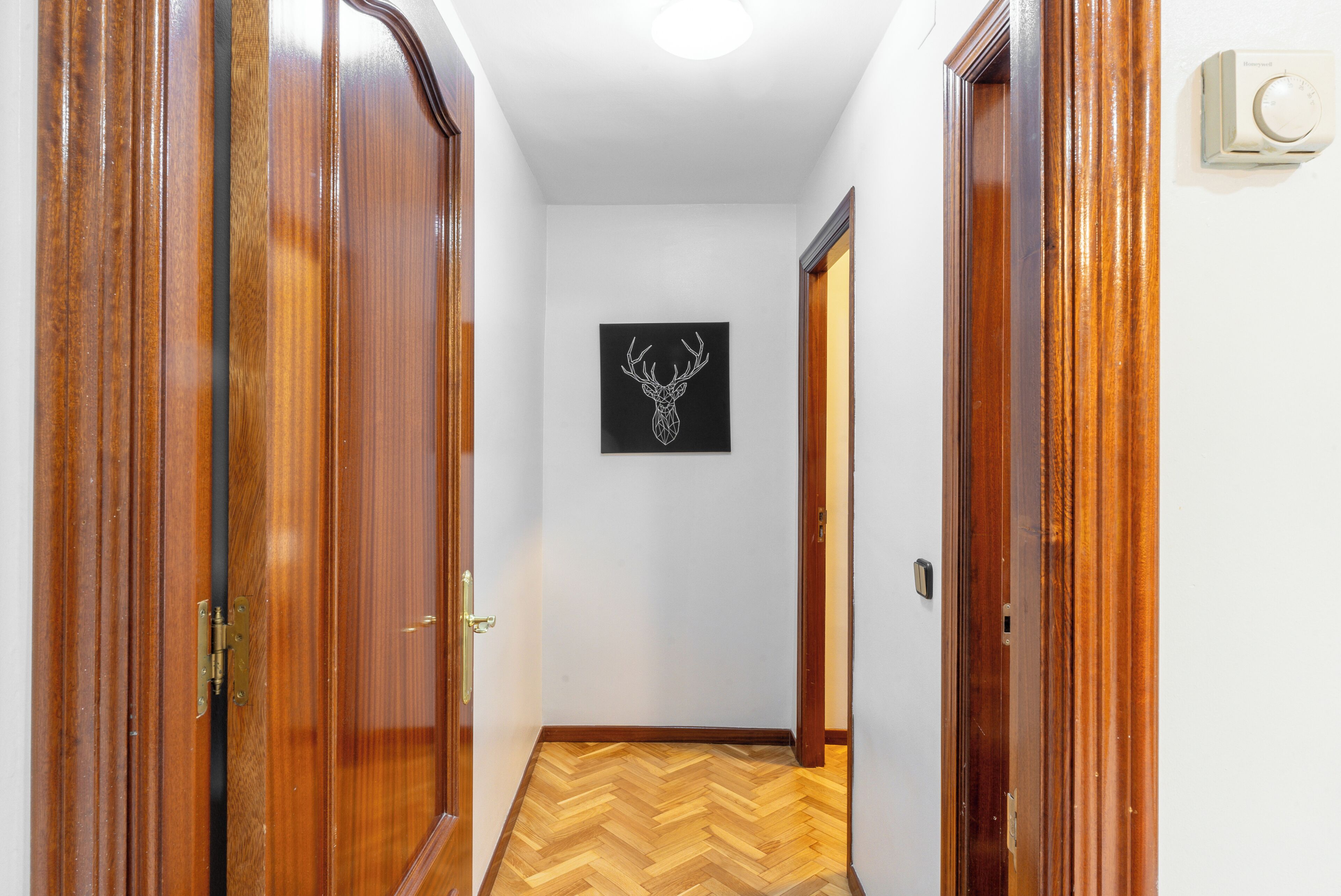 A hallway with wooden doors, a herringbone floor, and a deer head artwork on the wall.