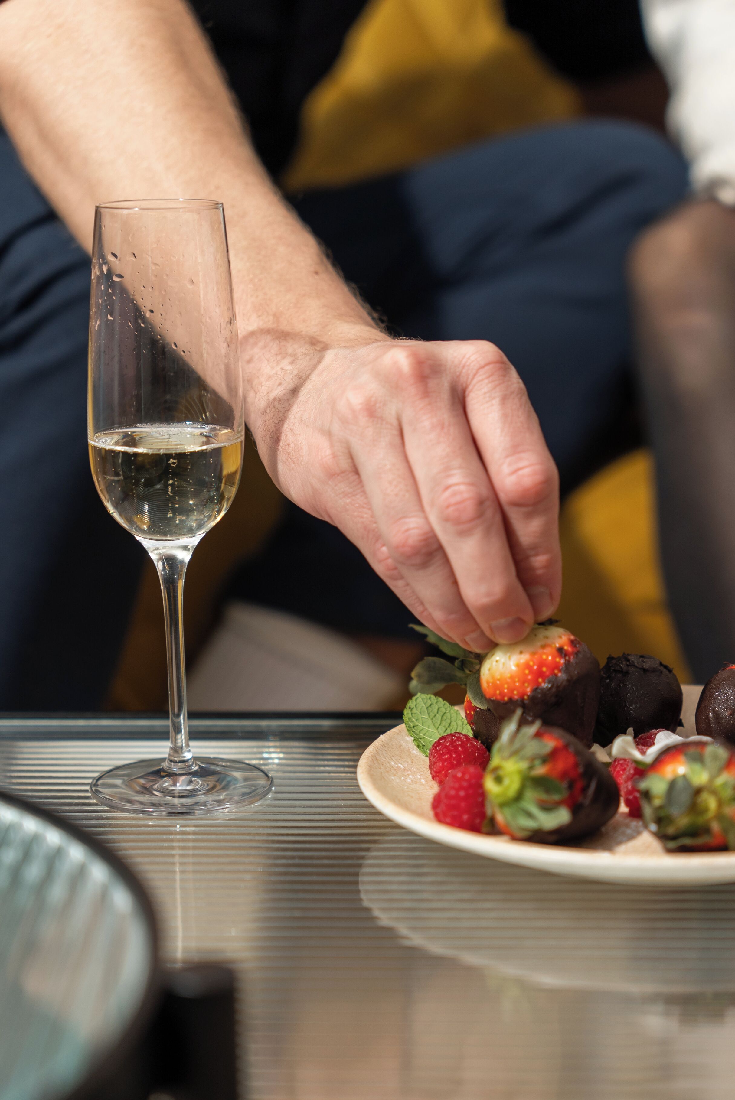 A person holding a glass of white wine, with a plate of strawberries and chocolate-covered strawberries in front of them.