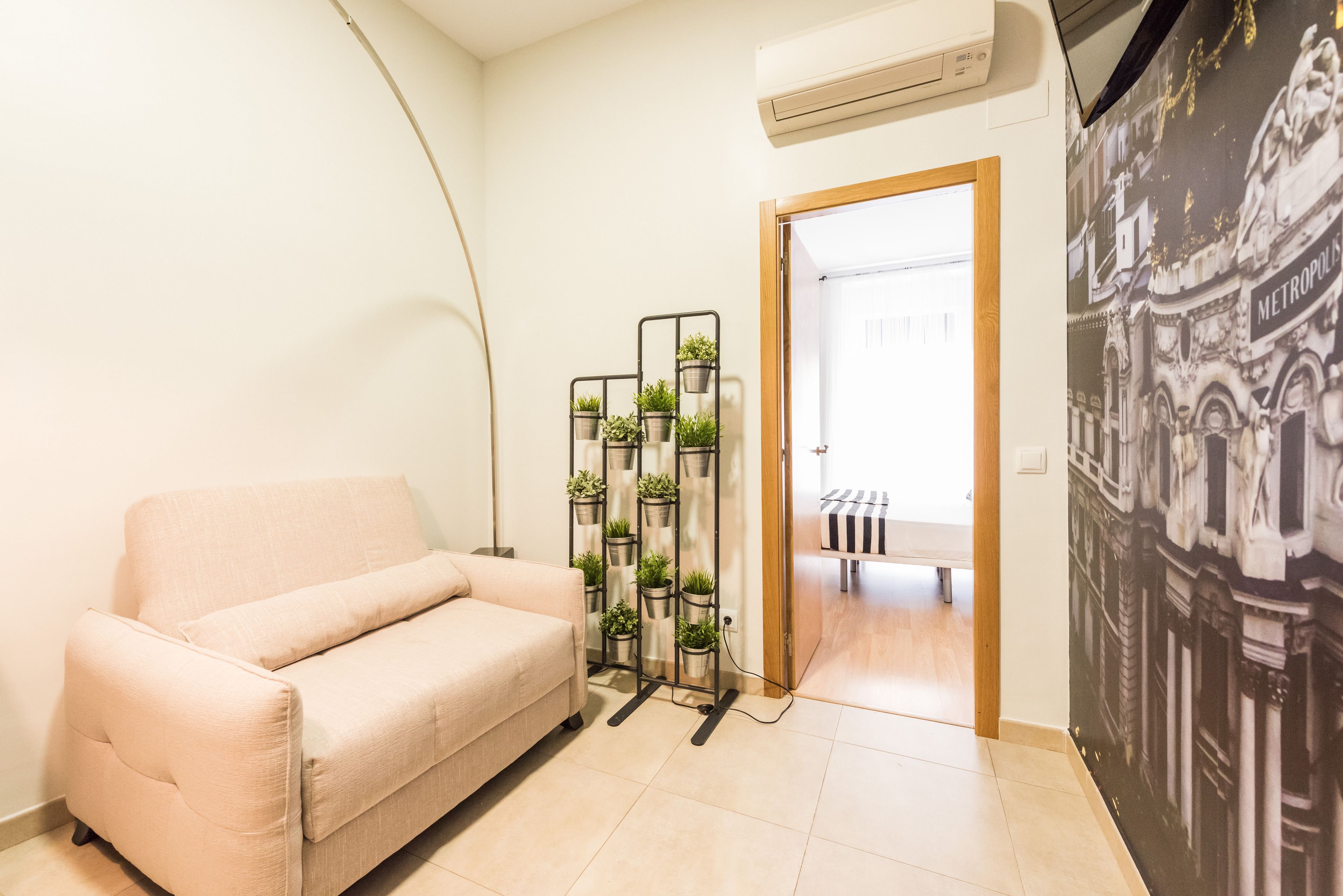 A living room with a beige sofa, a plant stand, and a wall mural.