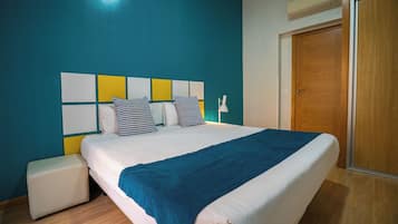 A neatly made bed with a blue blanket, a bedside table, and a wooden wardrobe in a room with teal walls.