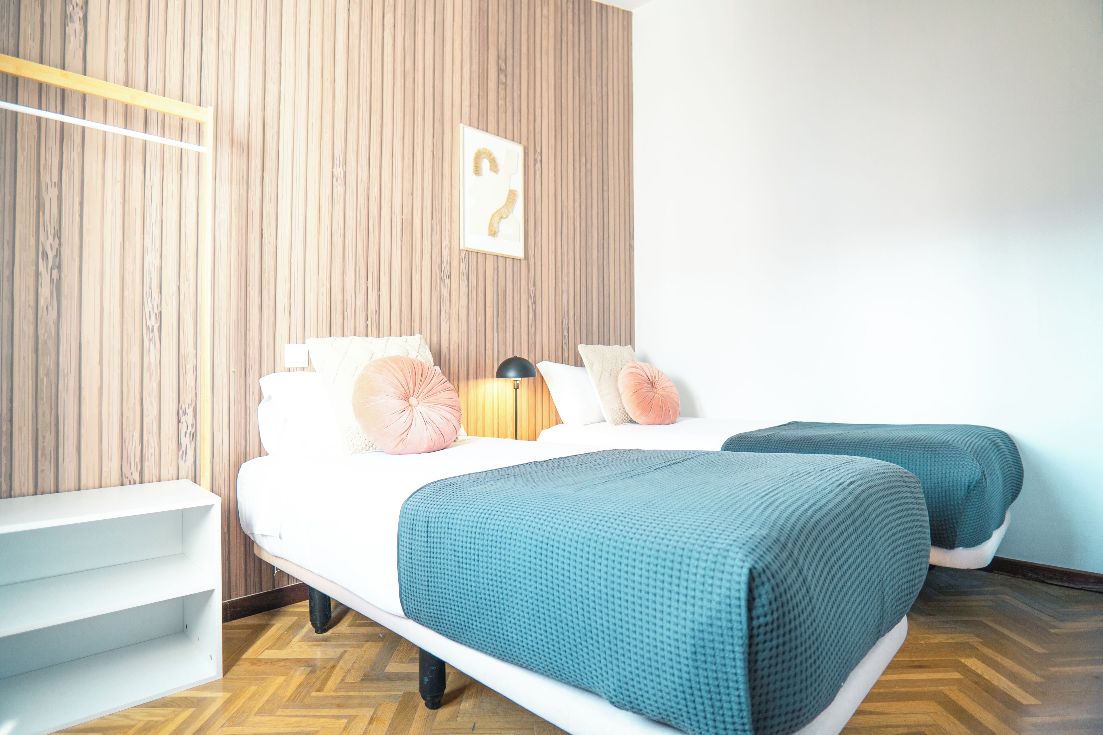 Un dormitorio con dos camas, una pared de madera, un estante blanco y una lámpara de pared.